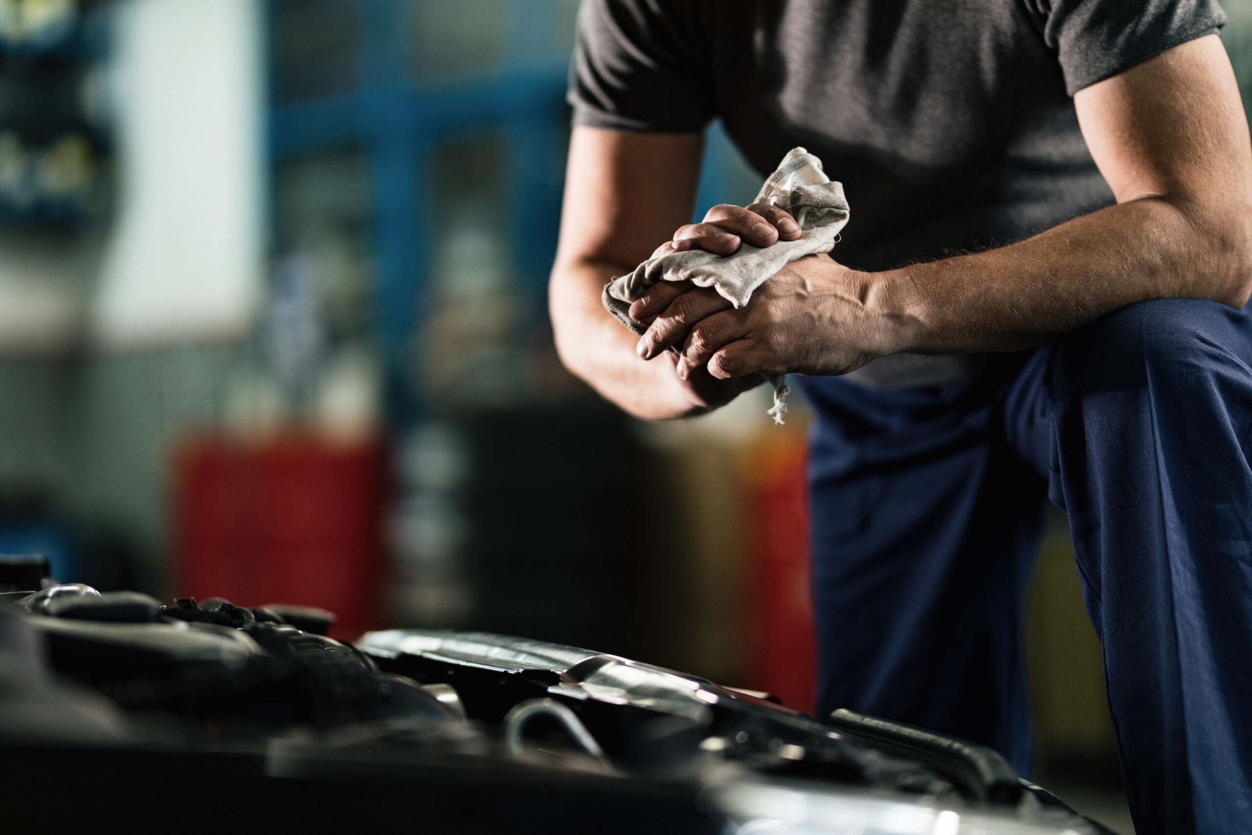 unrecognizable auto mechanic wiping his hands in a repair shop.